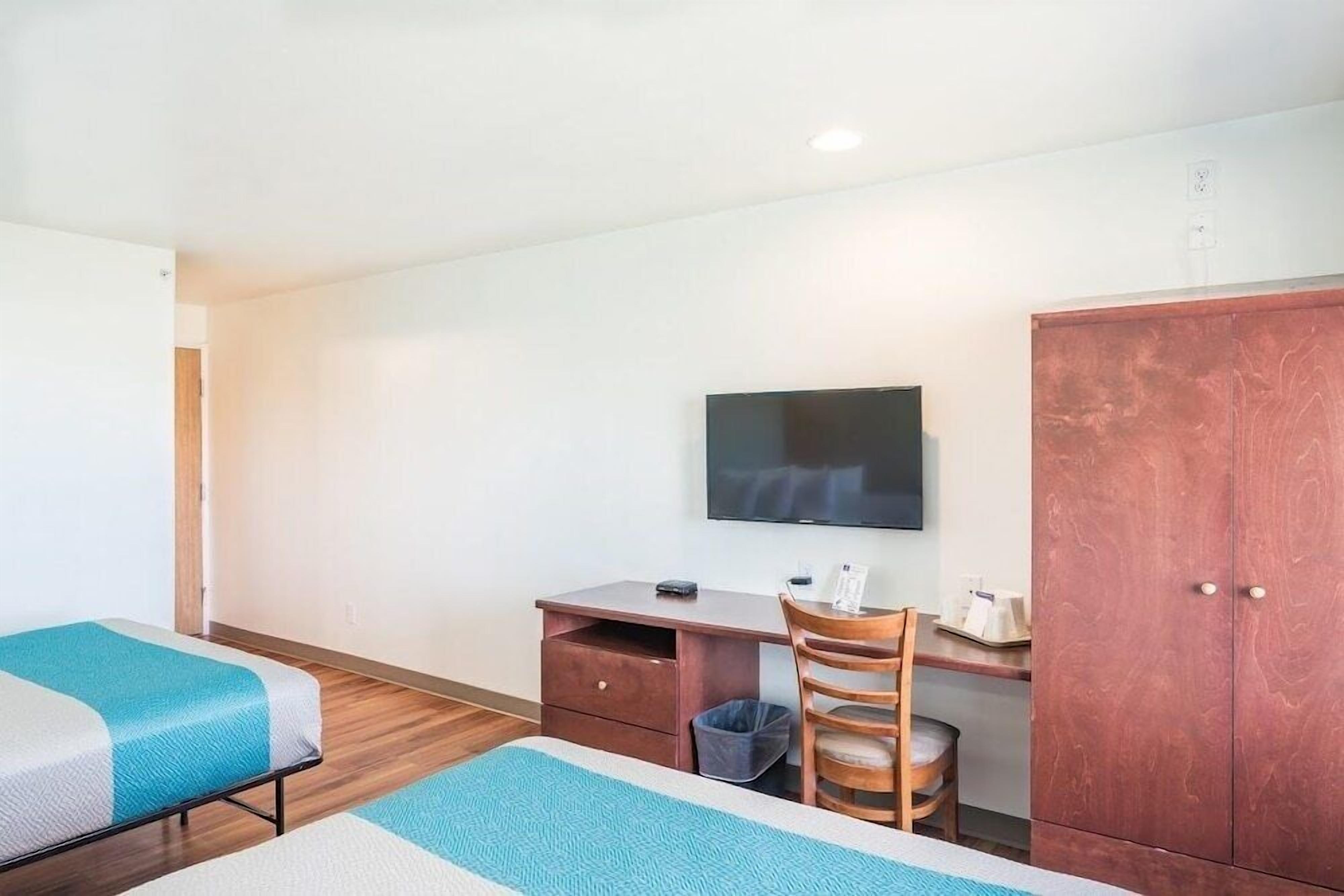 A hotel room with two beds, a desk with a chair, a television, and a wardrobe.