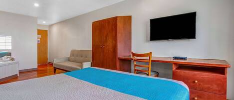 A bedroom with a bed, a desk, a chair, a wardrobe, and a TV.