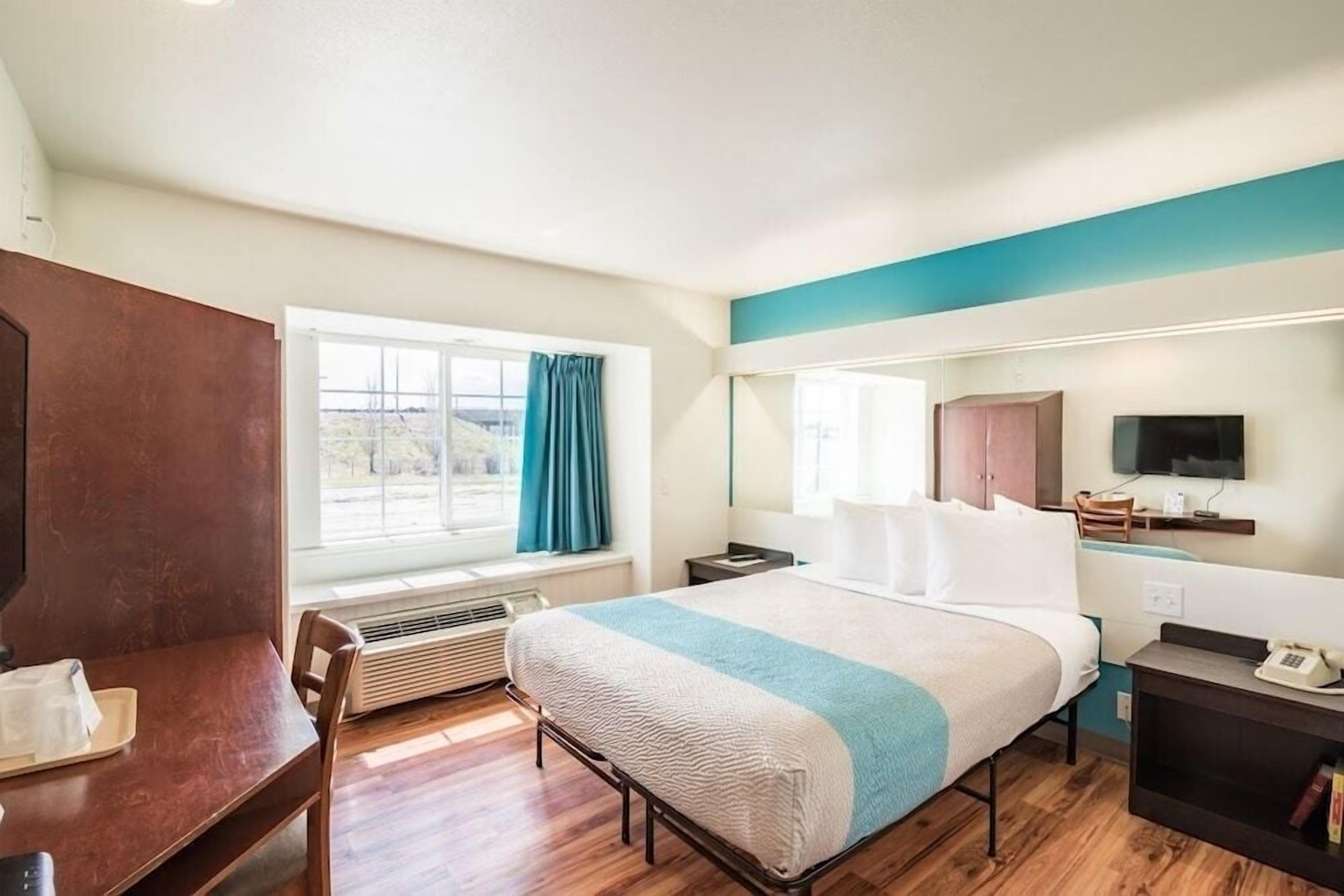 Ein Hotelzimmer mit Bett, Schreibtisch, Sessel, Fernseher und einem fenster mit Vorhängen.