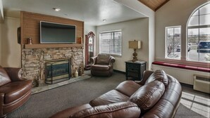 A living room with a stone fireplace, leather sofas, a television mounted above the fireplace, and a large window with a view of the outside. - Motel 6 Idaho Falls, ID - Snake River (Idaho Falls)