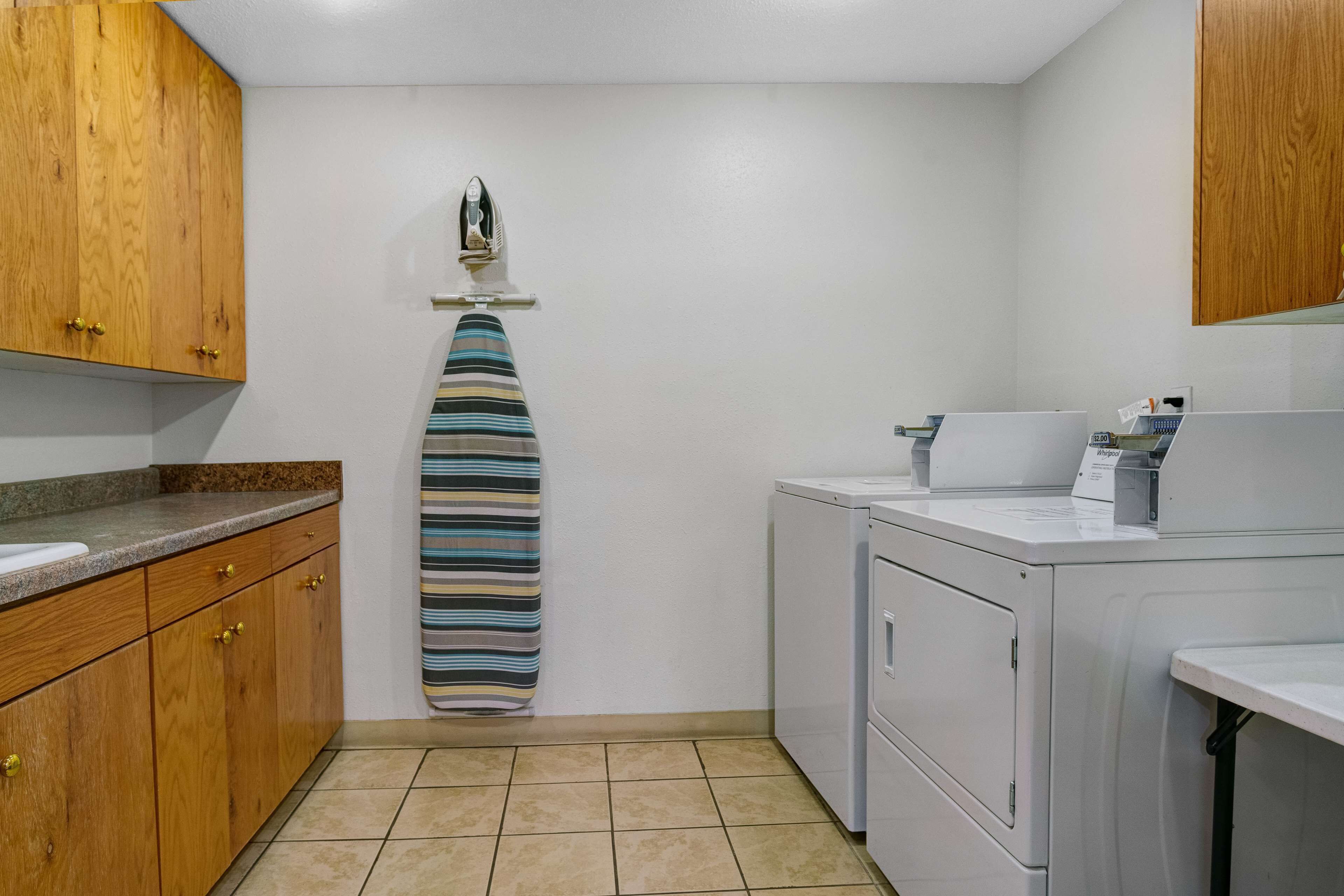 Une cuisine avec des meubles de rangement en bois, une serviette rayée suspendue à un porte-serviettes, un lave-linge et un plan de travail avec un évier.
