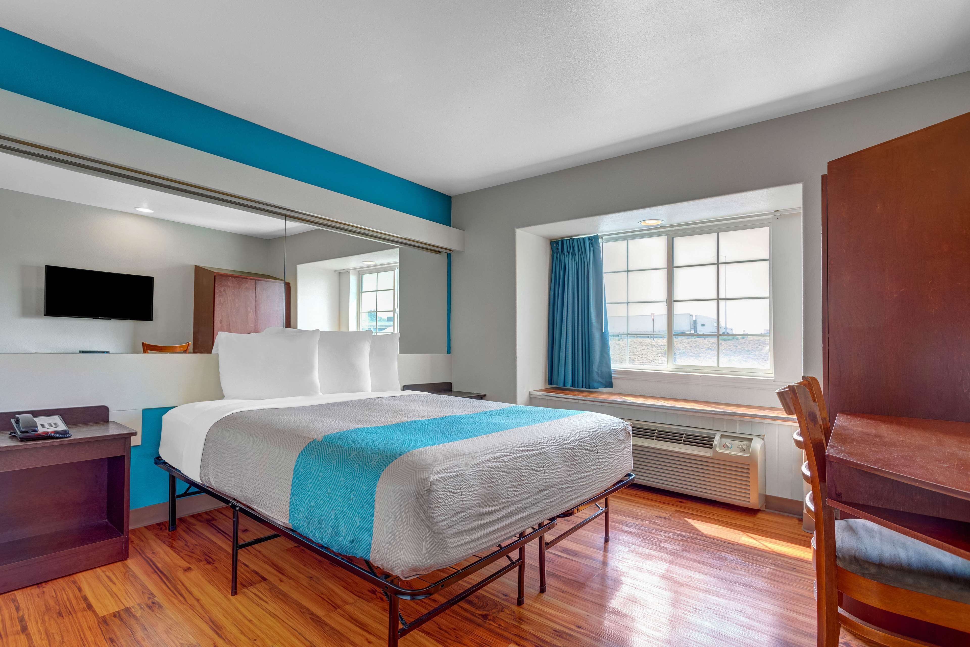 A modern hotel room with a bed, a desk, a chair, a TV, a window with curtains, and a view of the outside.