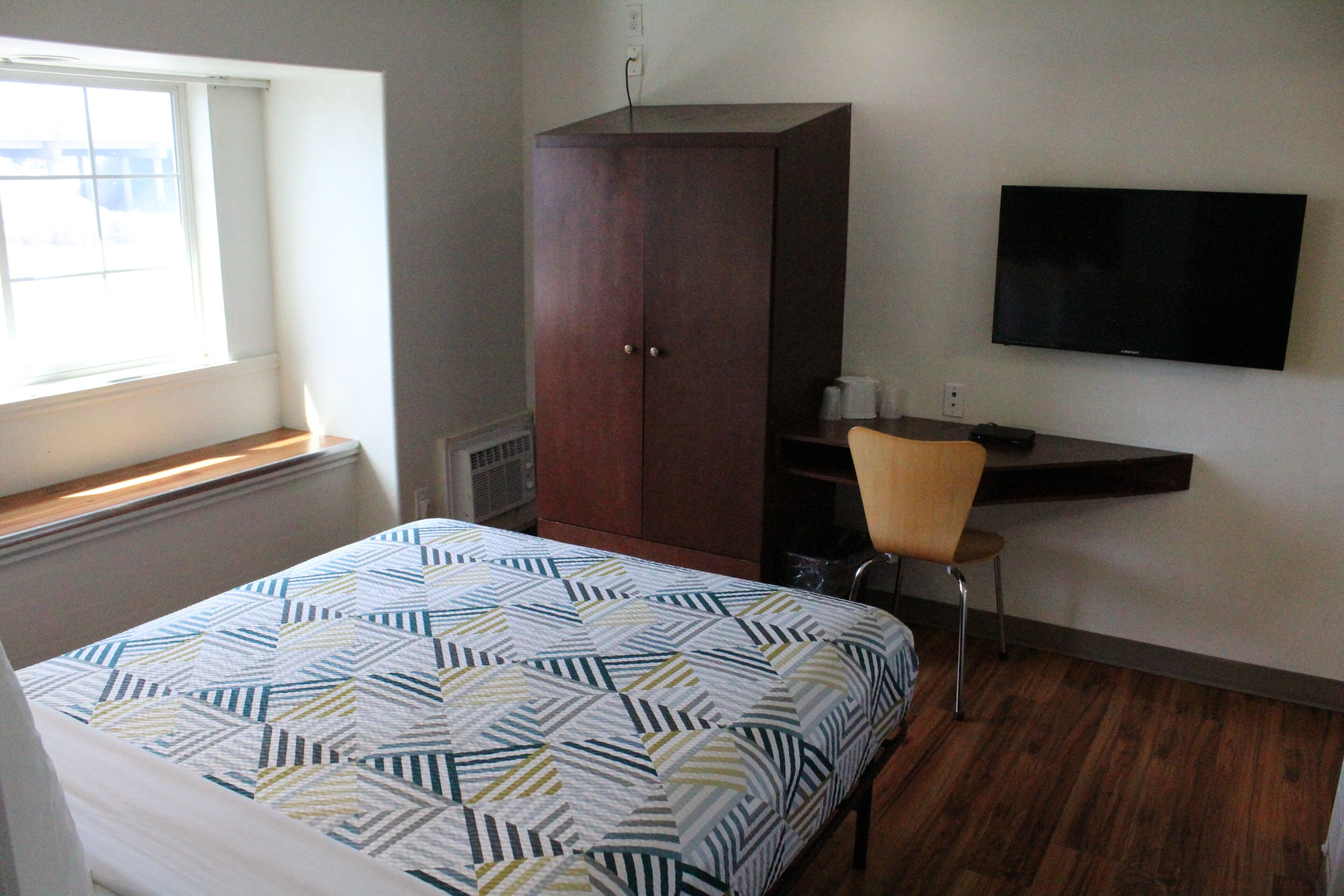 Un dormitorio con cama, armario, escritorio con silla, televisor y ventana.