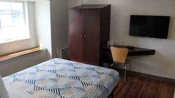 Un dormitorio con cama, armario, escritorio con silla, televisor y ventana.