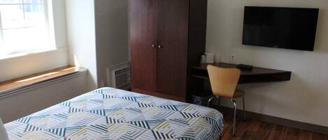 Un dormitorio con cama, armario, escritorio con silla, televisor y ventana.