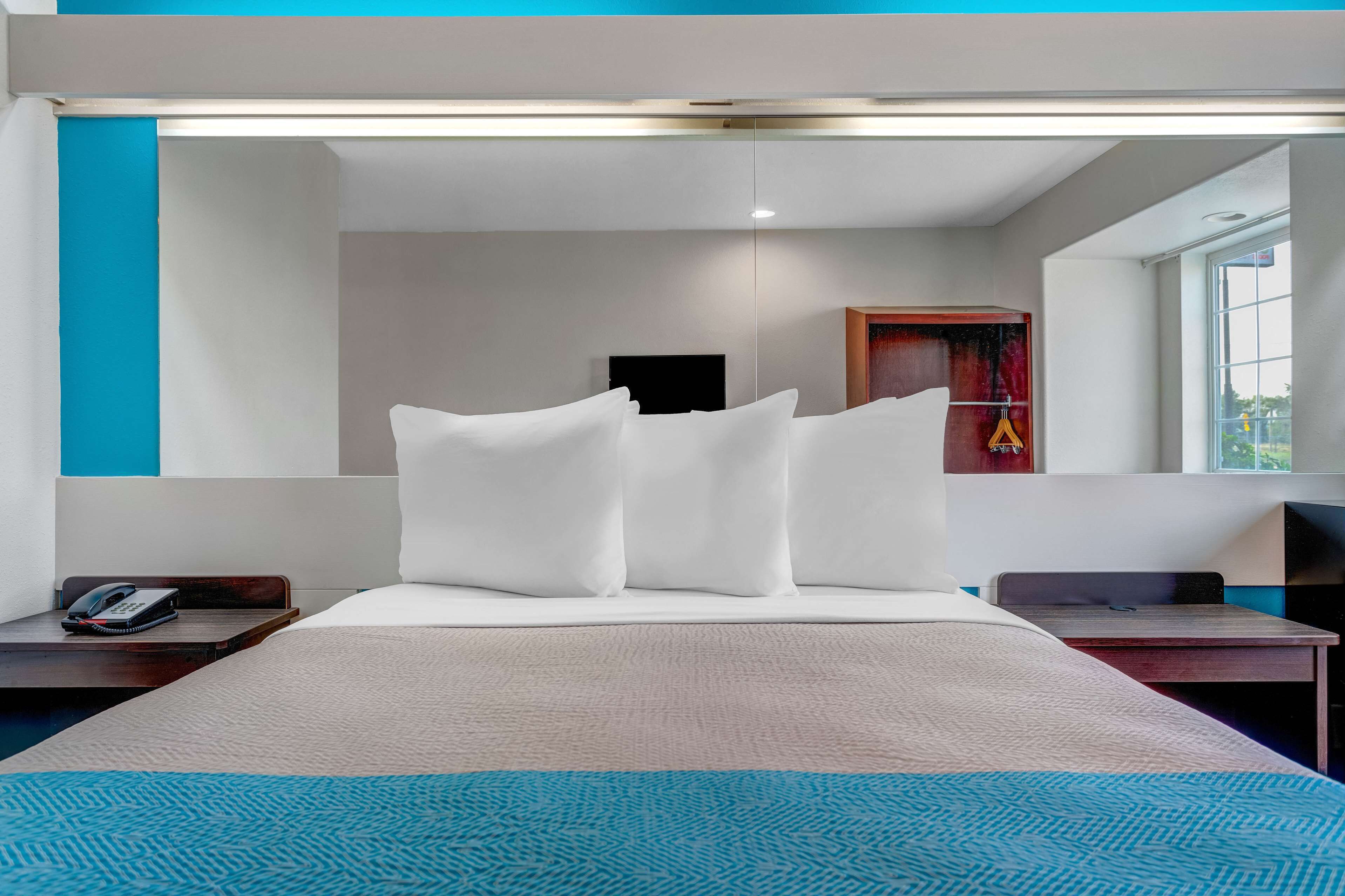 Quarto de hotel moderno com uma cama grande, uma mesa de cabeceira com telefone, uma mesinha e uma janela com vista.