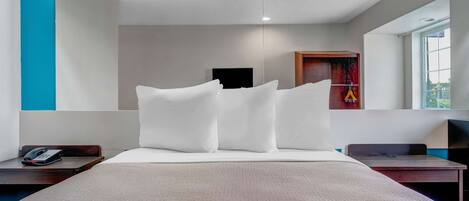 Quarto de hotel moderno com uma cama grande, uma mesa de cabeceira com telefone, uma mesinha e uma janela com vista.