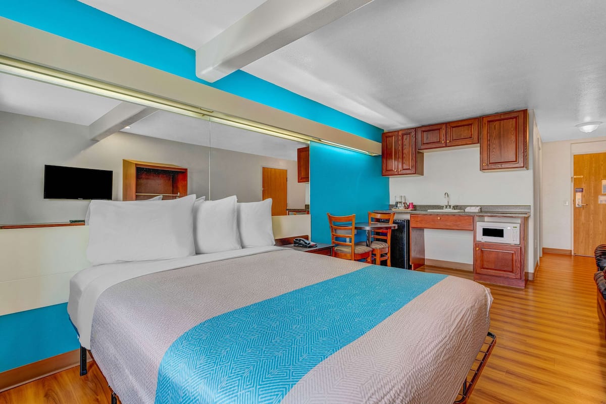 Ein Hotelzimmer mit Bett, Schreibtisch, Stuhl, Fernseher und einer Küchenzeile.