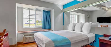 A hotel room with a bed, a desk, a chair, a window with curtains, and a TV on the wall.