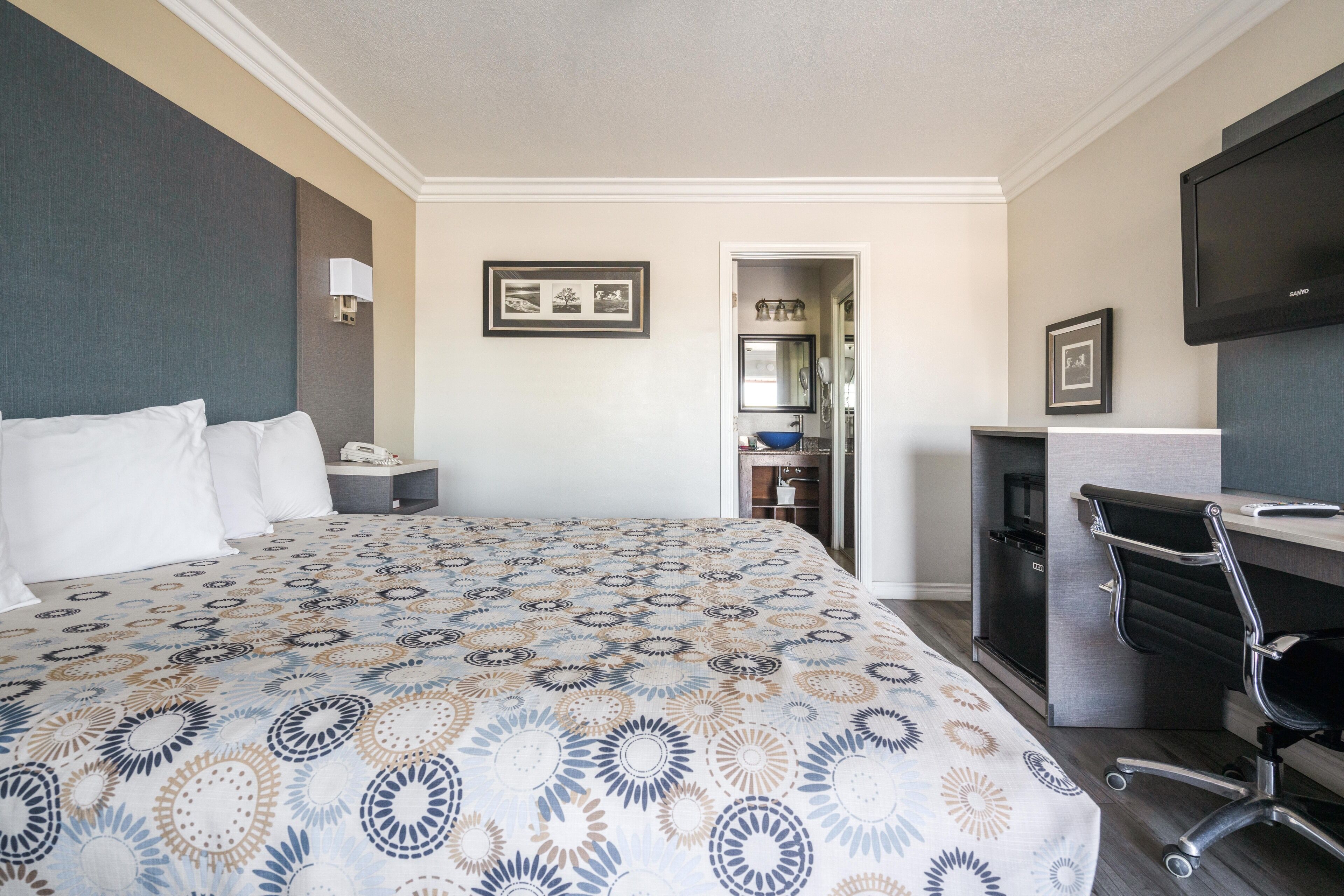 Ein Hotelzimmer mit einem großen Bett, einem Schreibtisch mit Stuhl, einem Fernseher und einem durchgegangene Tür erkennbaren Badezimmer.
