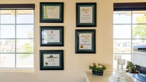 A wall with framed certificates and a vase of white roses. - Solaire Inn & Suites (Santa Maria)