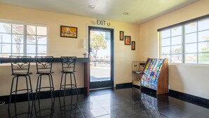 A lobby with a reception desk, three black bar stools, an exit sign, framed artwork, and a magazine rack. - Solaire Inn & Suites (Santa Maria)