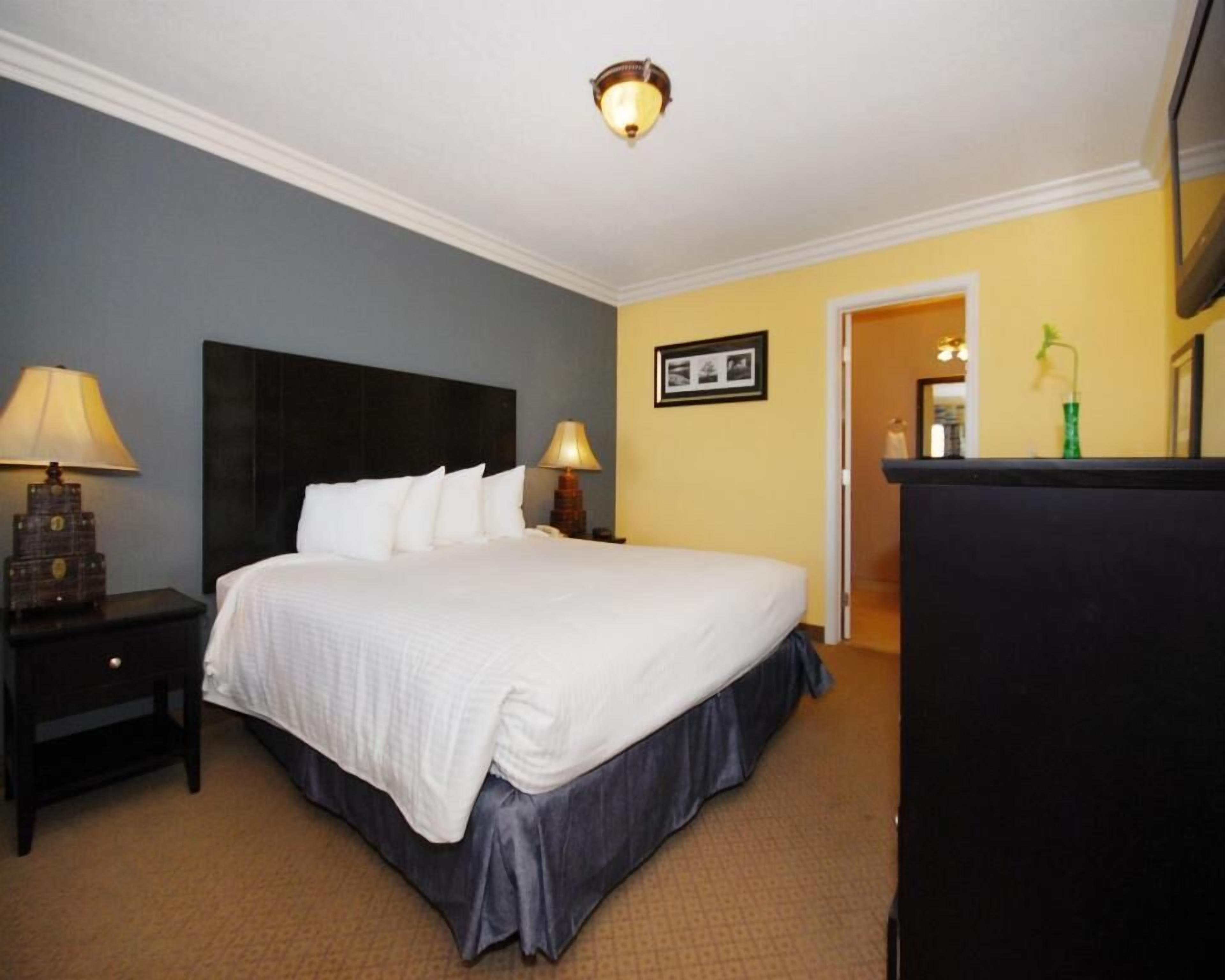 A hotel room with a large bed, two bedside lamps, a nightstand, a dresser, and a framed picture on the wall.