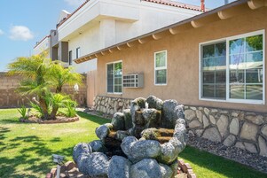 A house with a stone exterior, large windows, and a small garden with a rock feature.
