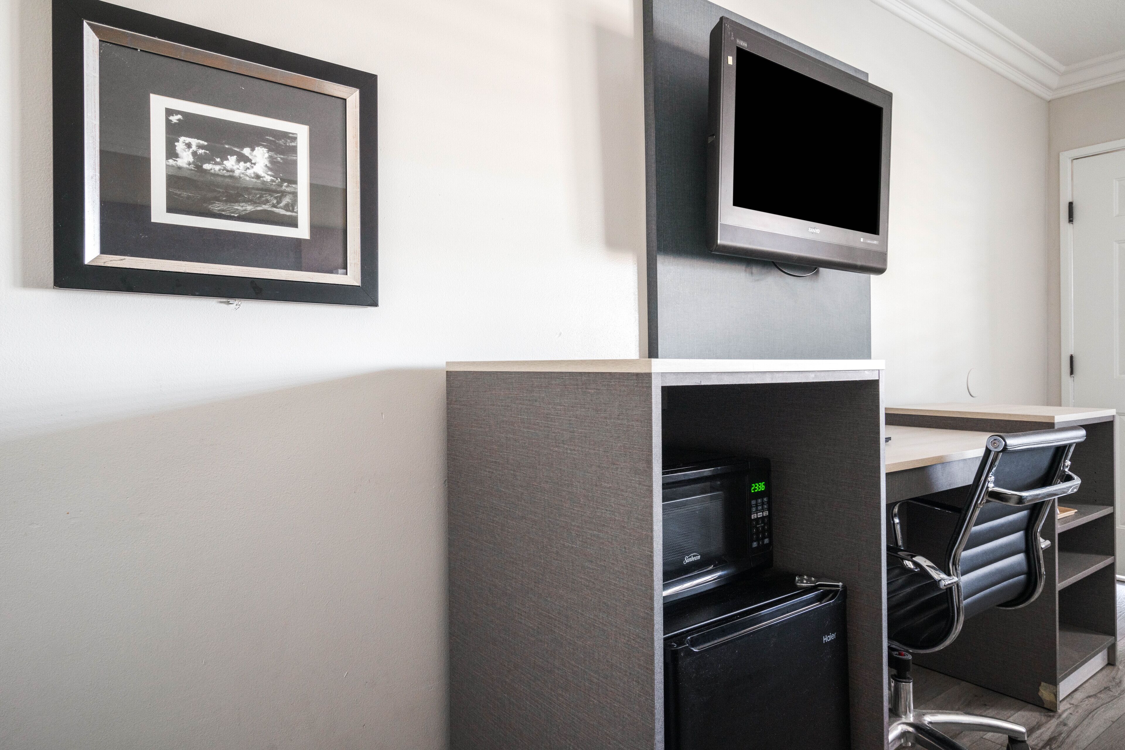 Une chambre d’hôtel moderne équipée d’un téléviseur à écran plat fixé à un meuble, d’un tableau encadré au mur et d’un four encastré.