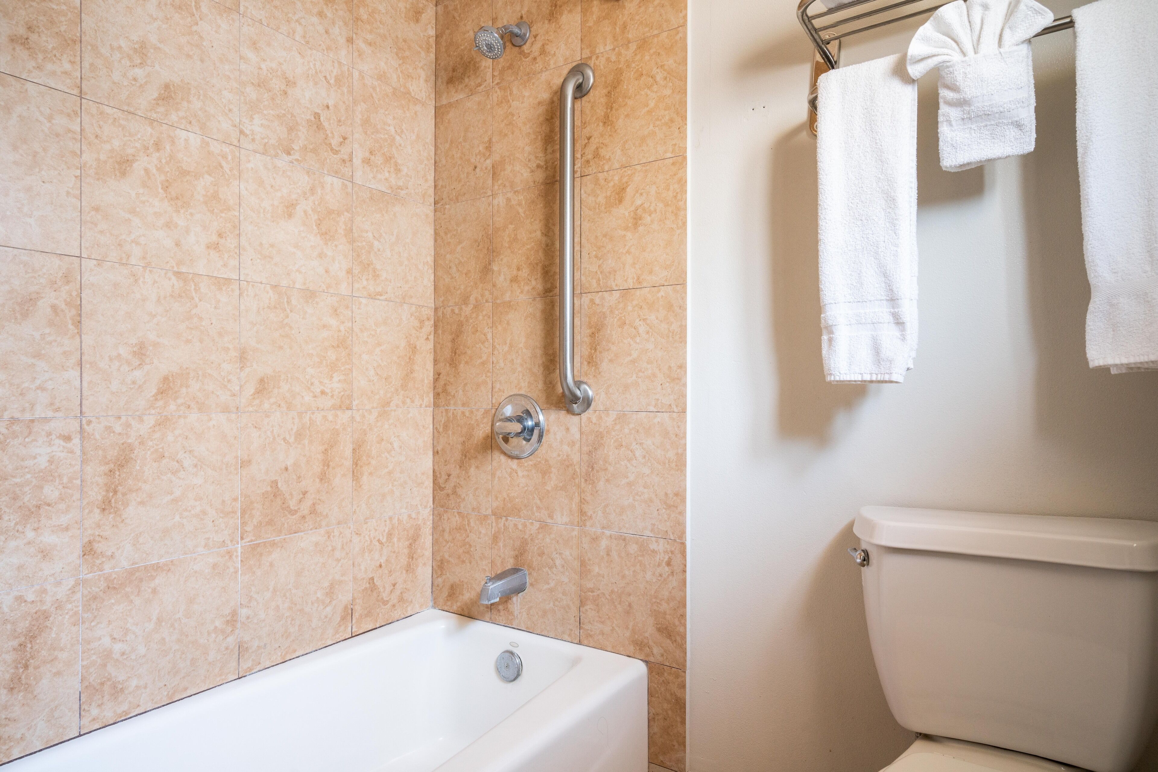 Une salle de bain avec des carreaux de couleur beige, une baignoire, des toilettes et un porte-serviettes avec des serviettes.