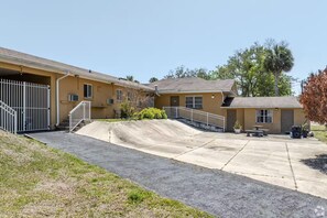 A building with a ramp leading to a covered area, a small patio with a table and chairs, and a fenced driveway. - Lumina Motel (Daytona Beach)