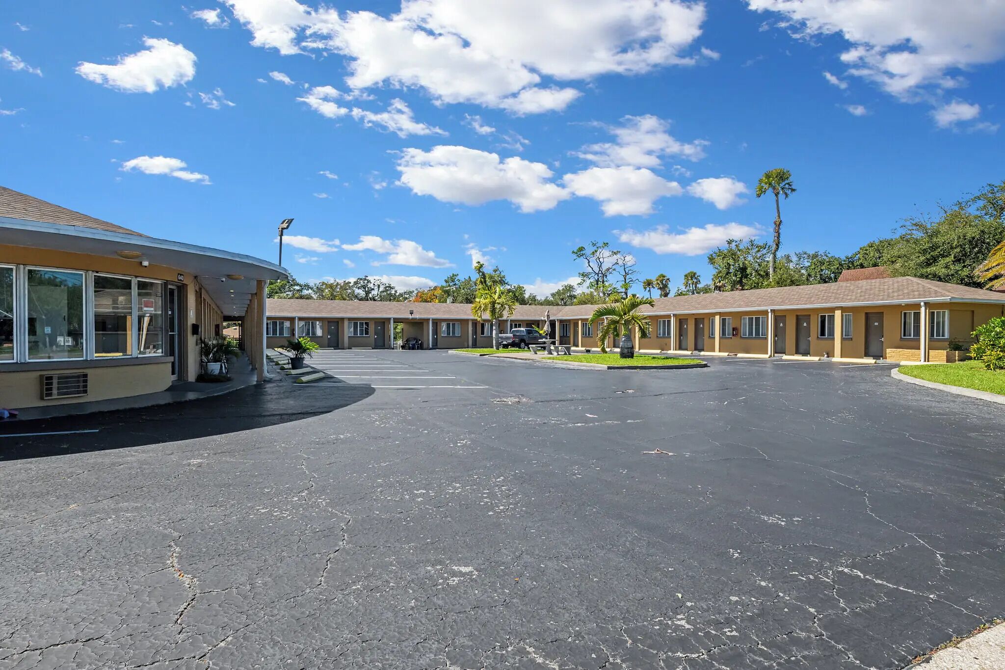 A motel with a large parking lot, multiple motel units, and a building with large windows on the left.