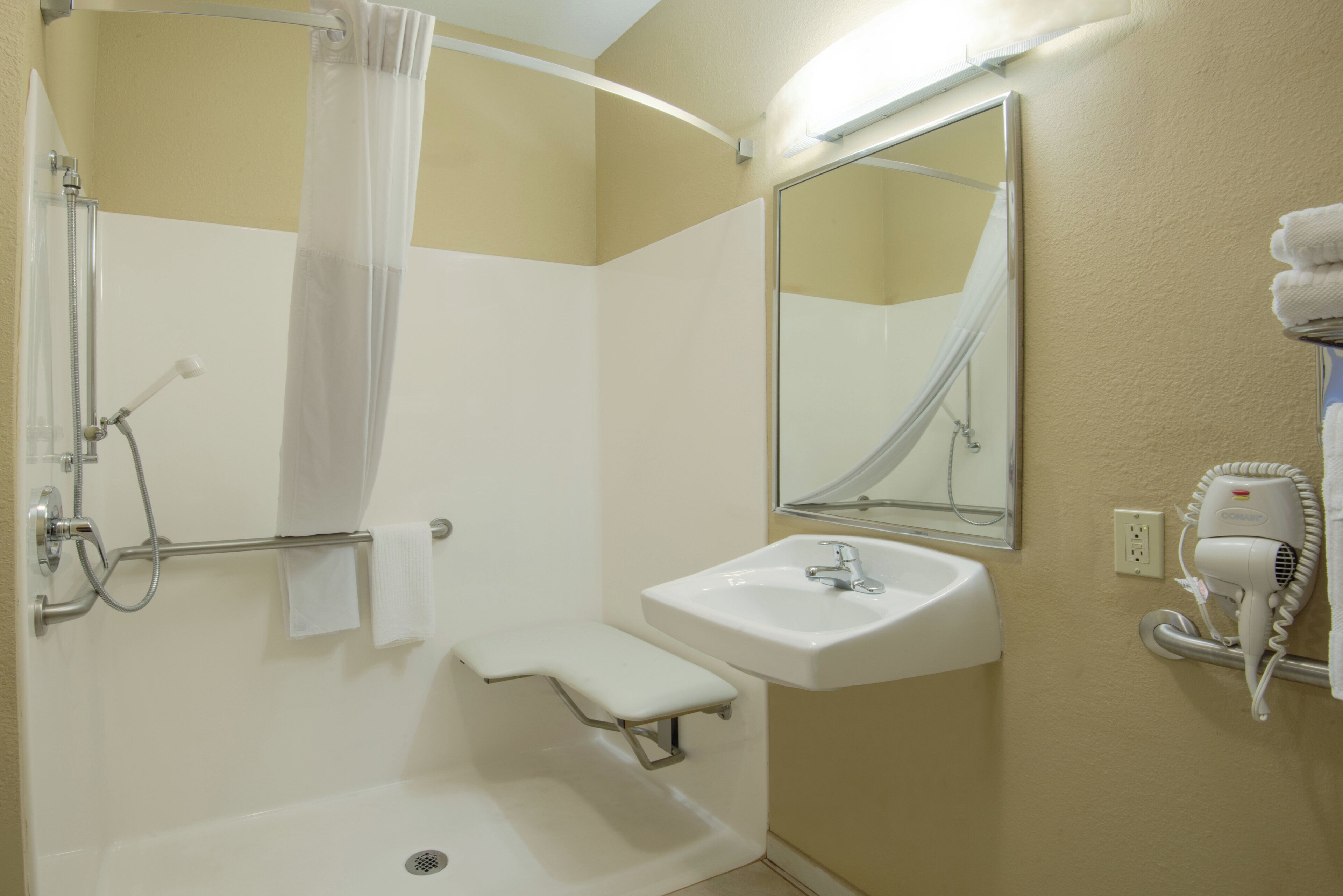 Un baño con ducha, lavamanos y un secador de pelo fijado a la pared.