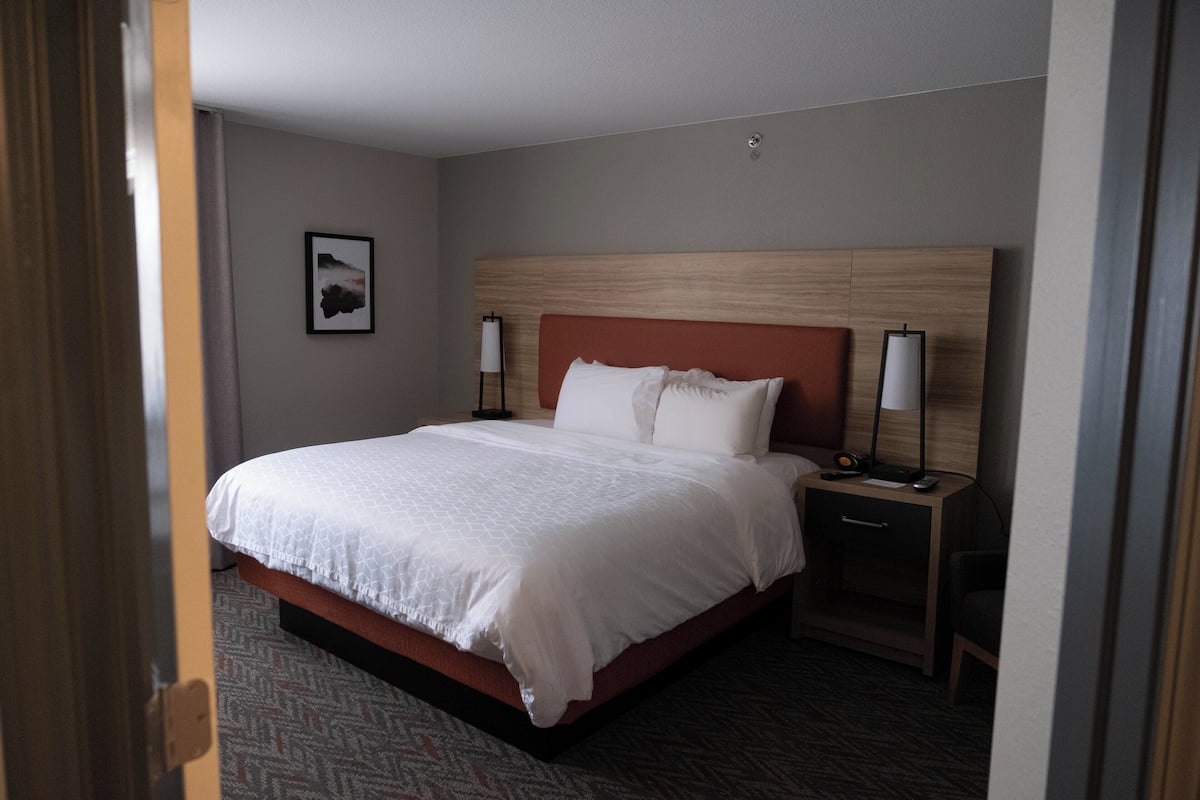 A hotel room with a large bed, a wooden headboard, two bedside tables with lamps, a small drawer, and a patterned carpet.