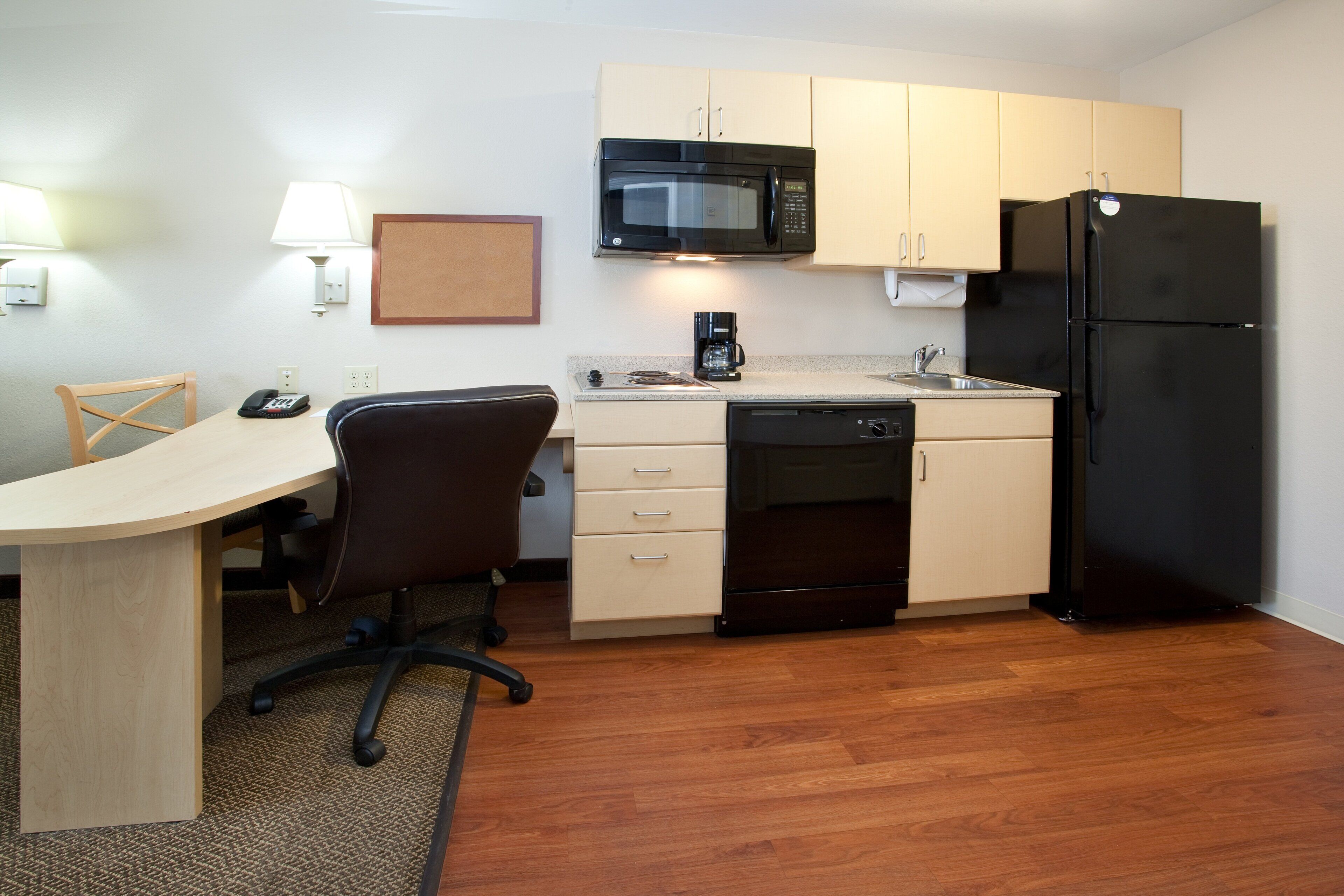 A compact kitchen with a microwave, refrigerator, coffee maker, and a small dining area with a chair and table.