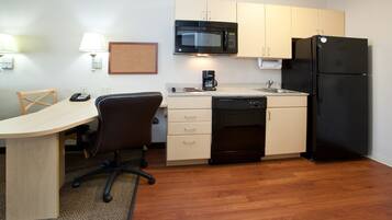 A compact kitchen with a microwave, refrigerator, coffee maker, and a small dining area with a chair and table.