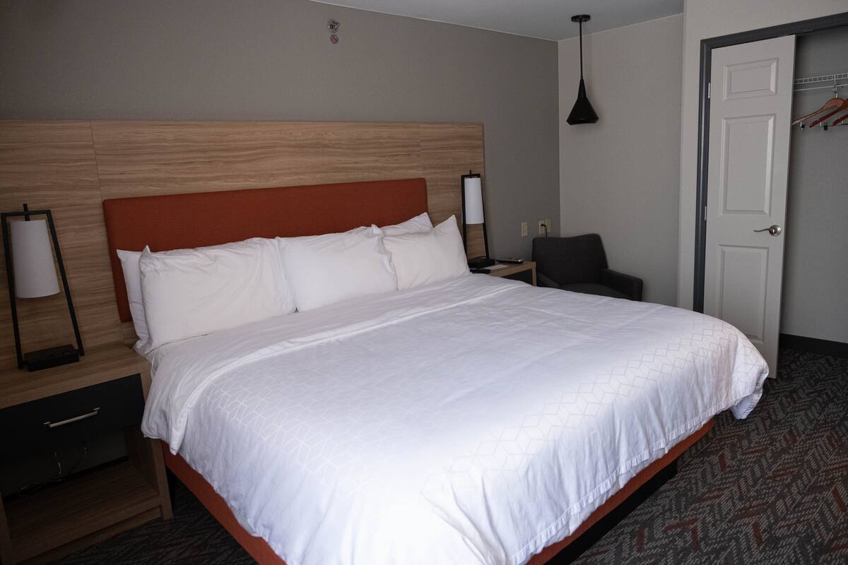 A hotel room with a large bed, a nightstand, a chair, a door, and a lamp.