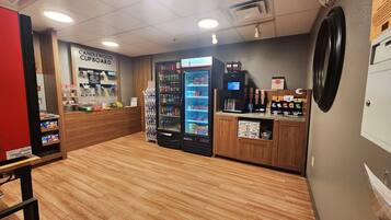 Interior de una cafetería con mostrador de madera, máquina expendedora de bebidas y vitrina refrigerada.