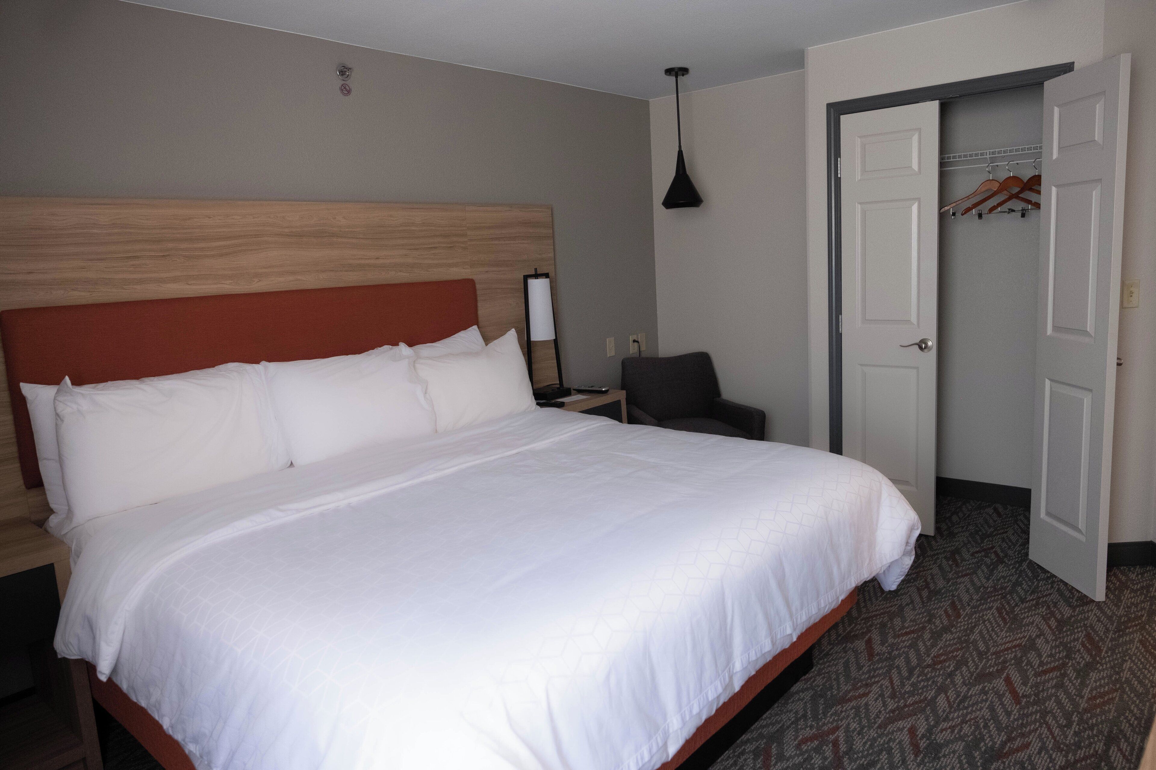 A hotel room with a large bed, a nightstand, a chair, a desk, and a door leading to a hallway.