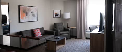 Una habitación de hotel con sofá, sillón, mesa de centro, lámpara y televisor.
