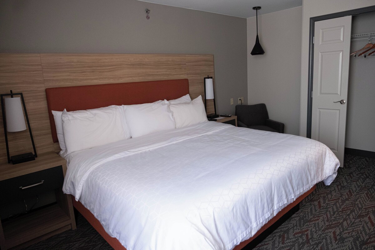 A hotel room with a large bed, a nightstand, a chair, a door, and a lamp.