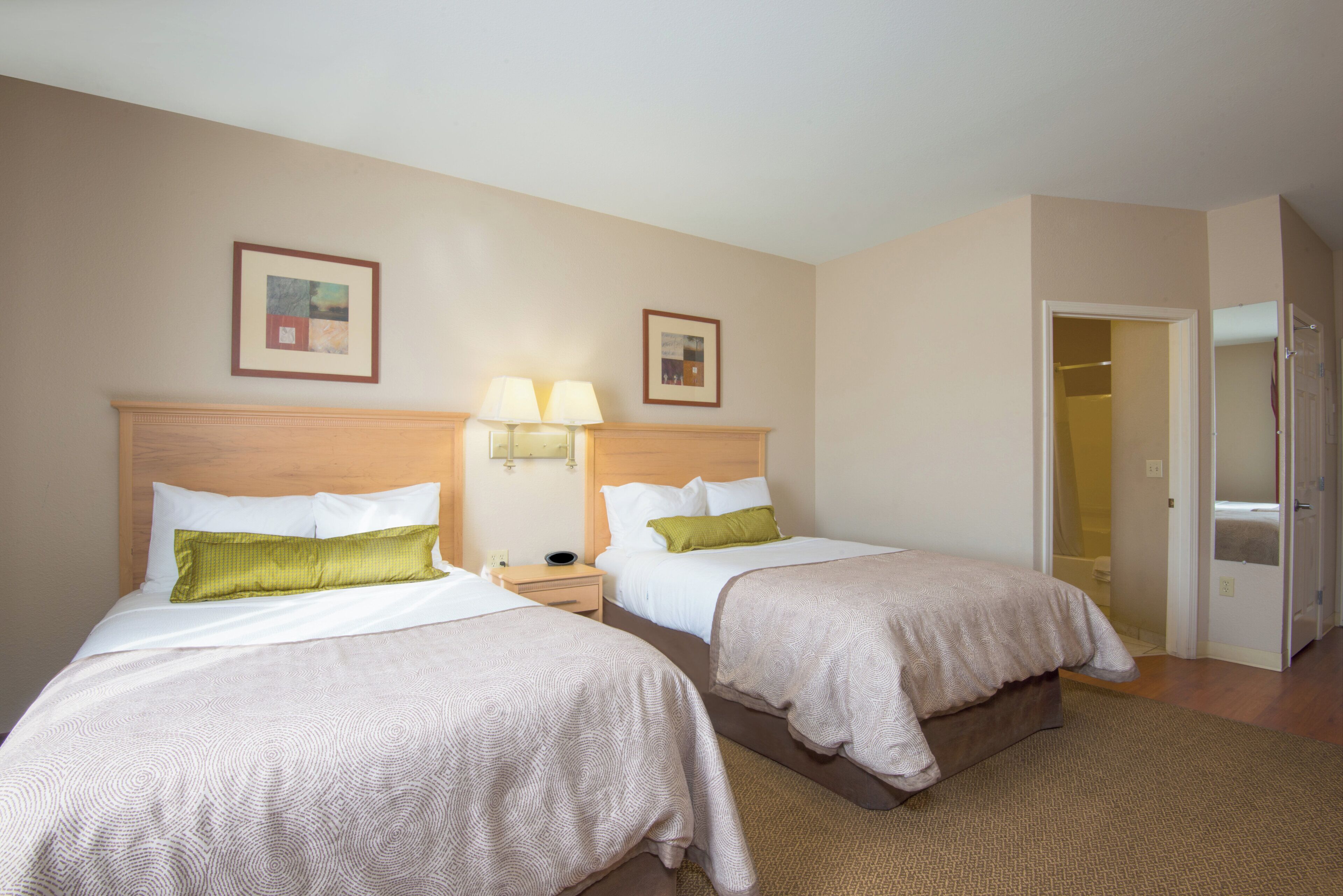 Une chambre d’hôtel avec deux lits, une table de chevet avec des lampes, une porte donnant sur une salle de bain et un tableau encadré au mur.