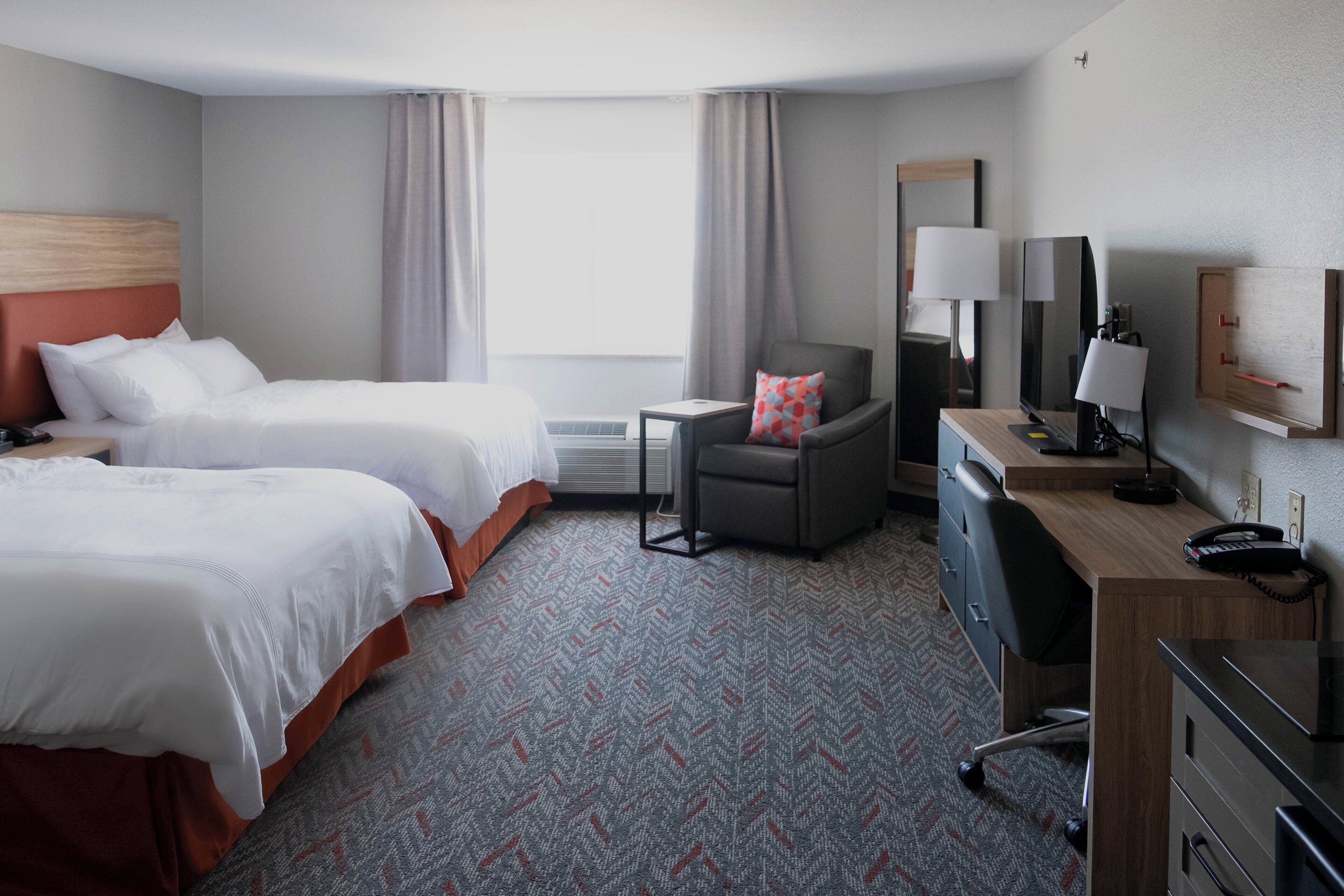 A hotel room with two beds, a desk with a telephone, a chair, a mirror, and a window with curtains.