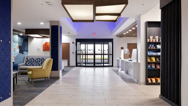 A hotel lobby with a reception desk, a seating area with a yellow armchair, and a snack bar with packaged goods. - Holiday Inn Express & Suites Kingsville by IHG (Kingsville)