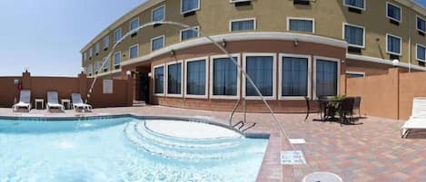 A hotel with a swimming pool, lounge chairs, and a patio area.