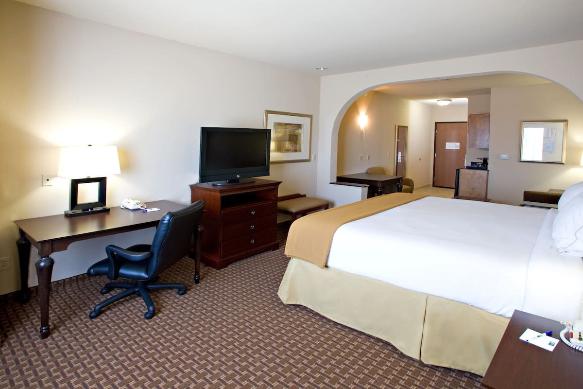 Une chambre d’hôtel équipée d’un lit, d’un bureau, d’une chaise, d’une télévision et d’une petite kitchenette.