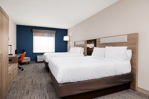 Quarto de hotel com duas camas, uma escrivaninha, uma cadeira e uma janela grande.