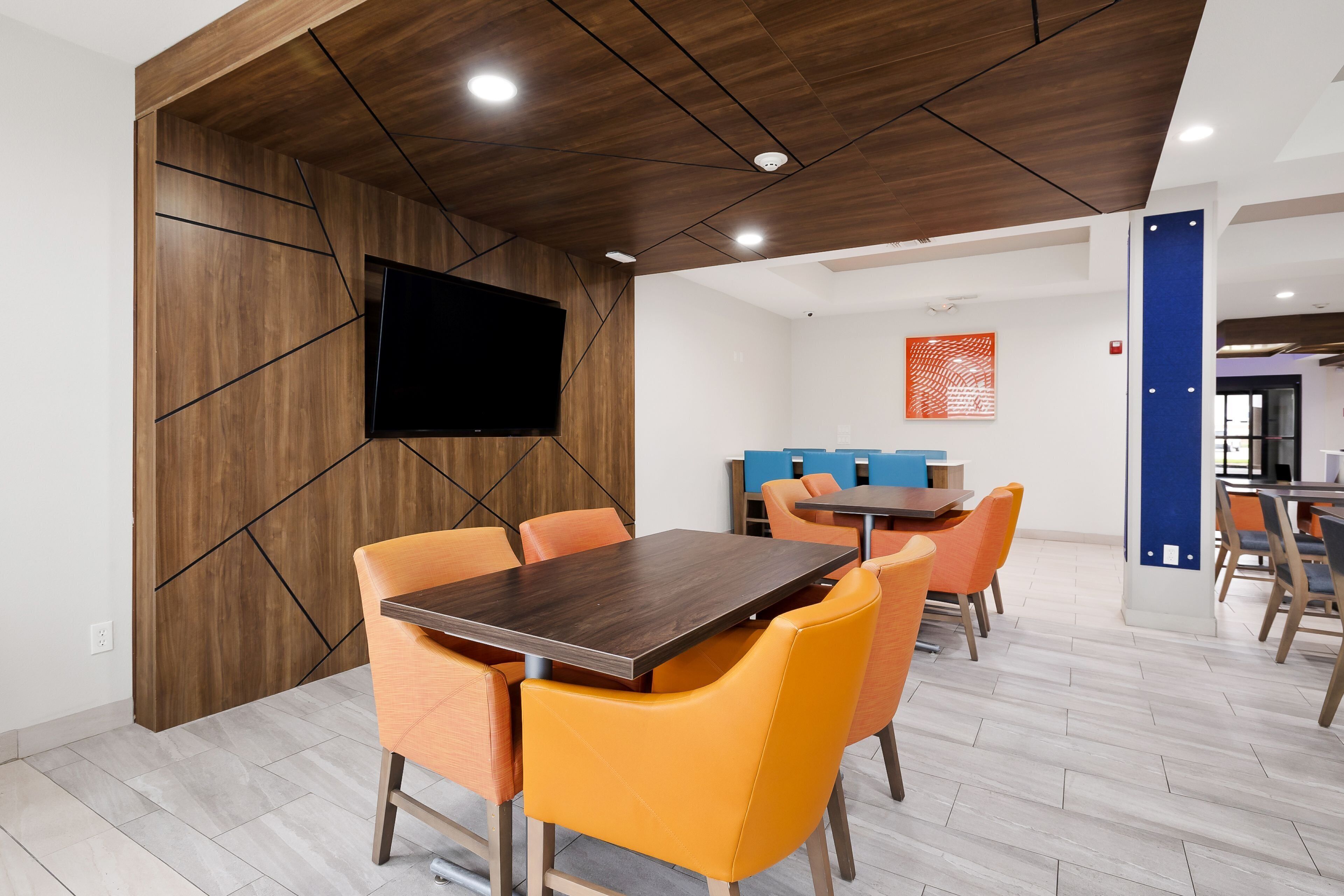 A modern conference room with a wooden accent wall, a flat-screen TV, and orange chairs around a dark wooden table.
