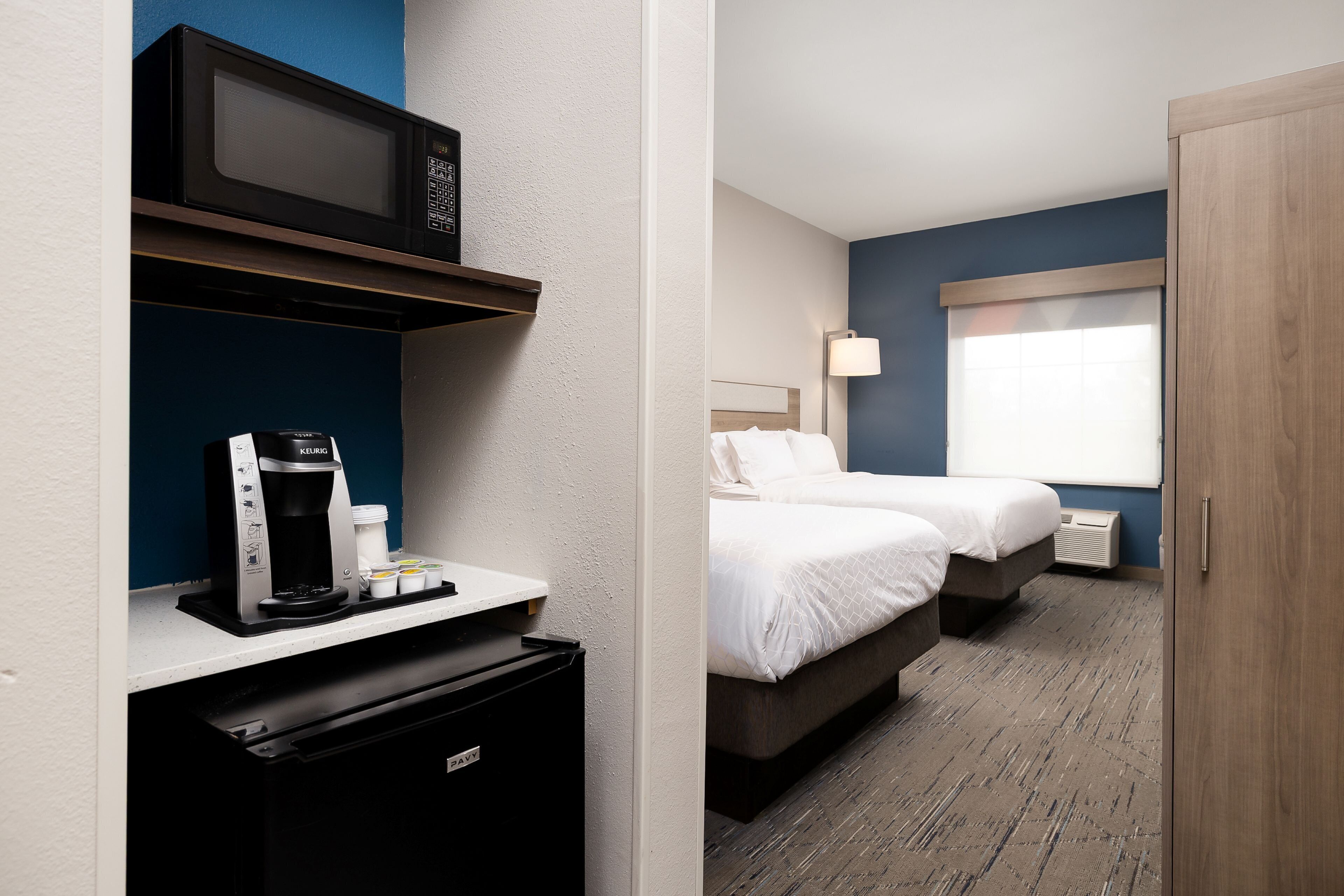 Une chambre d’hôtel avec une kitchenette, deux lits, une fenêtre avec des stores et une armoire en bois.