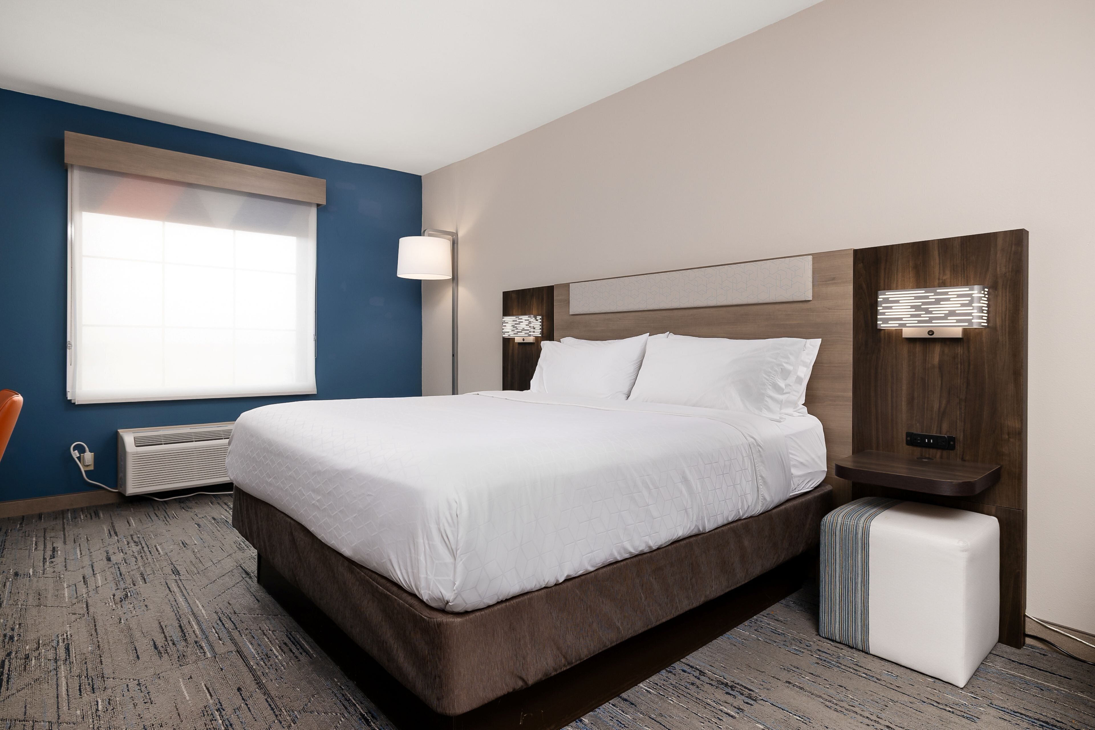 A hotel room with a large bed, a bedside table, a lamp, and a window.