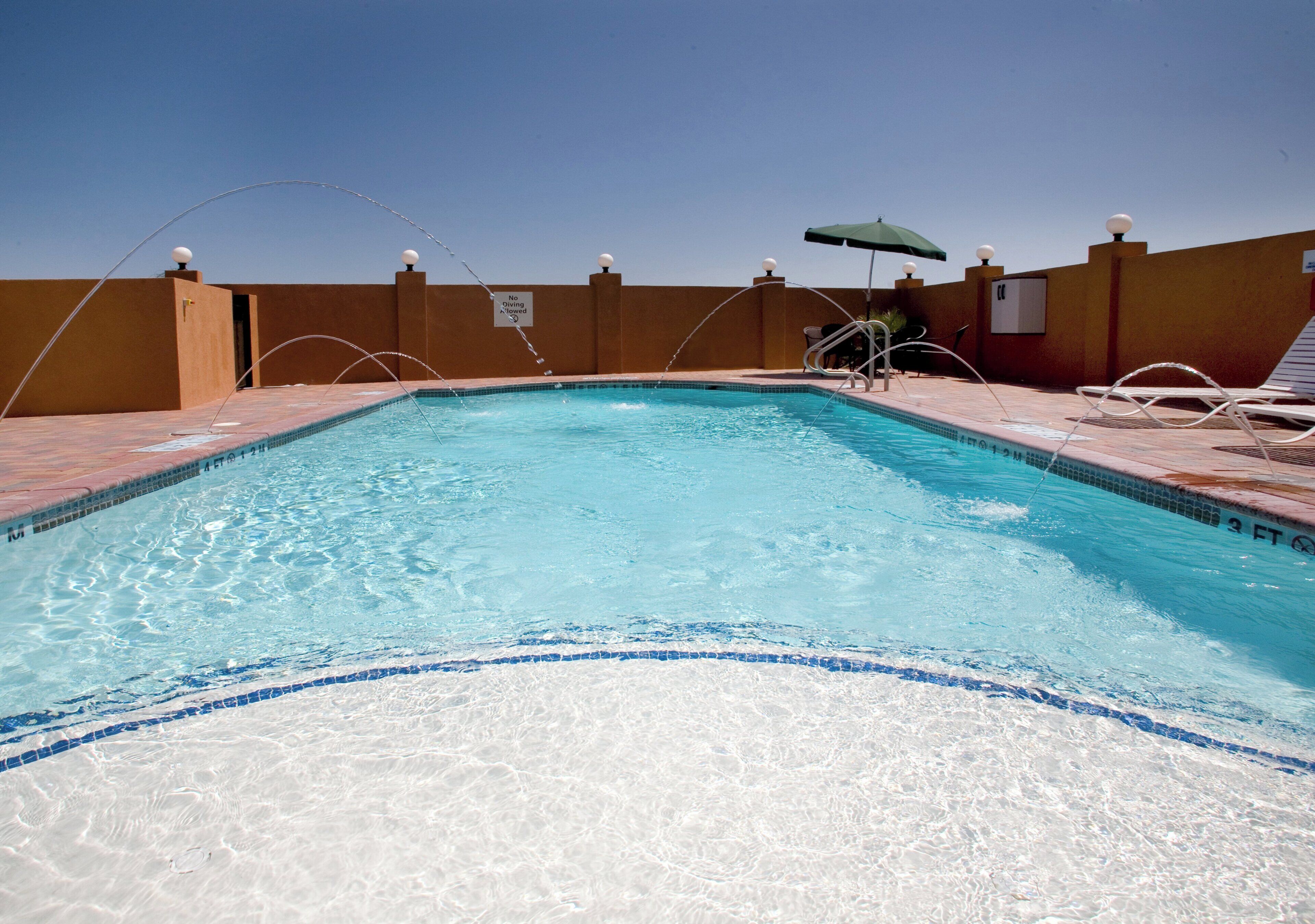 A swimming pool with clear blue water, surrounded by a tiled deck and a low wall.
