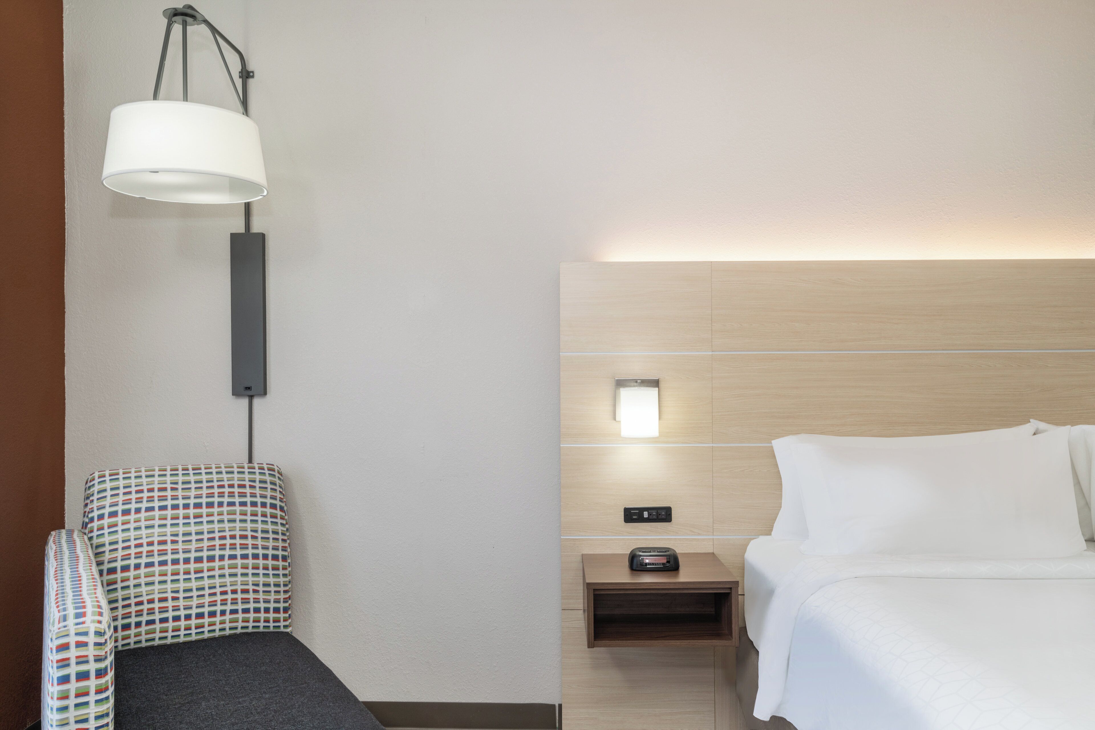 A hotel room with a bed, a bedside table, a lamp, and a chair.