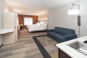 A hotel room with a bed, a sofa, a desk, a chair, and a kitchenette.
