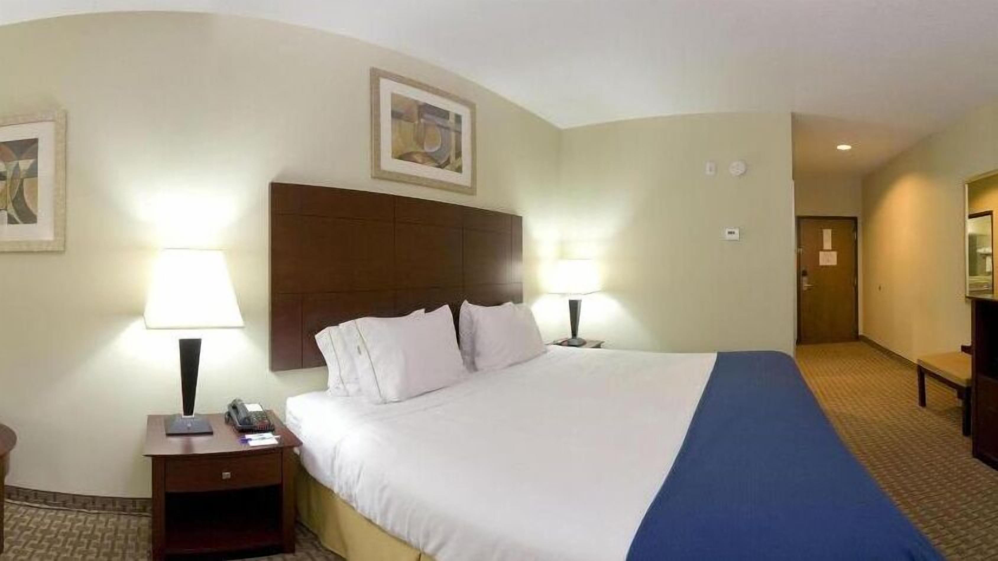 A hotel room with a large bed, two bedside lamps, a wooden headboard, and a framed picture on the wall.