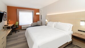 Hotellihuone, jossa on suuri sänky, työpöytä, tuoli, ikkuna ja seinään kiinnitetty valaisin.