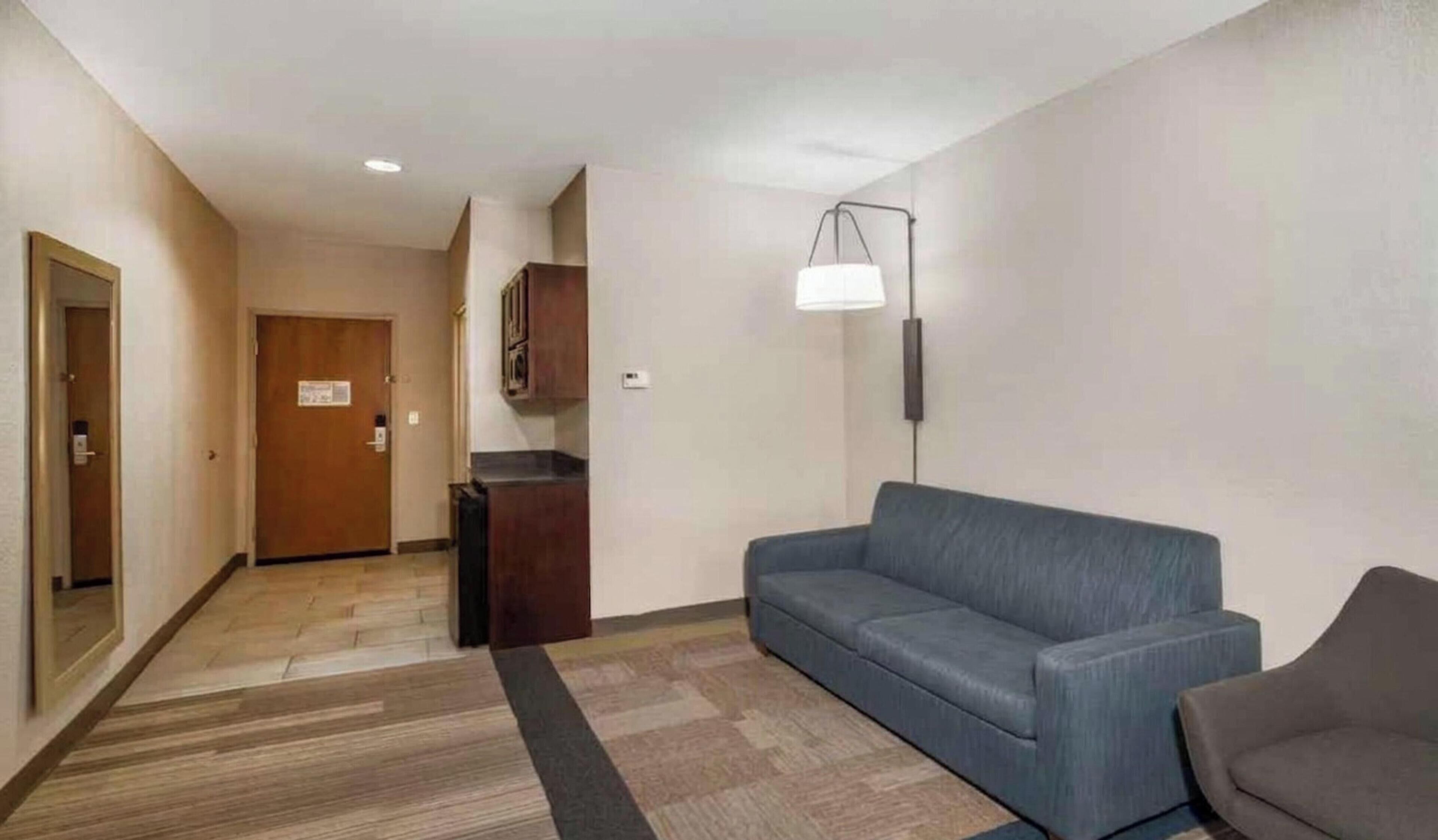 A hotel lobby with a wooden door, a dark-colored sofa, a small table, and a floor lamp.