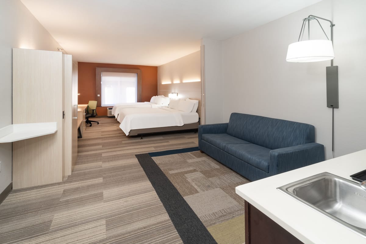 A hotel room with a bed, a sofa, a desk, and a kitchenette.