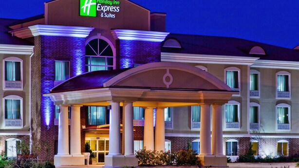Holiday Inn Express & Suites -hotellin rakennus, jossa on katettu sisäänkäynti, pylväät ja hyvin valaistu julkisivu.