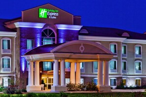 Een Holiday Inn Express & Suites gebouw met een overdekte ingang, zuilen en een goed verlichte gevel.