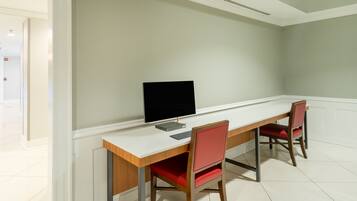 A room with a white desk, a computer monitor, and two red chairs.